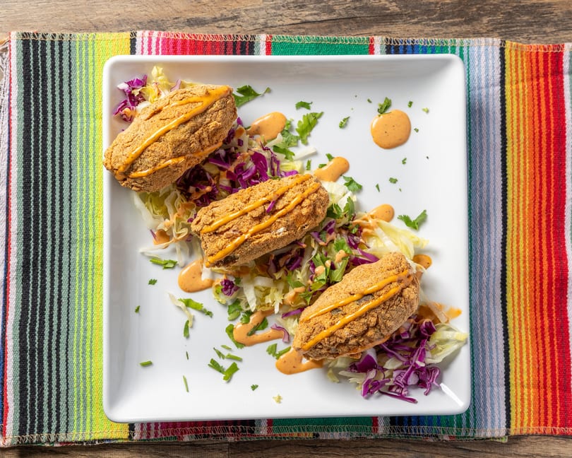 Three fried fish fillets drizzled with sauce, served on a bed of shredded lettuce and cabbage.