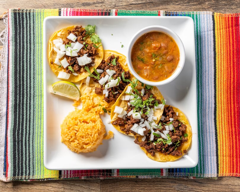 Four street tacos with ground beef, diced onions, and cilantro, served with rice and beans.